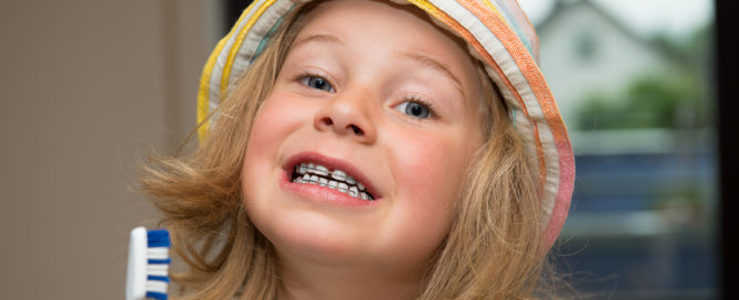 little girl with braces retainer and toothbrush