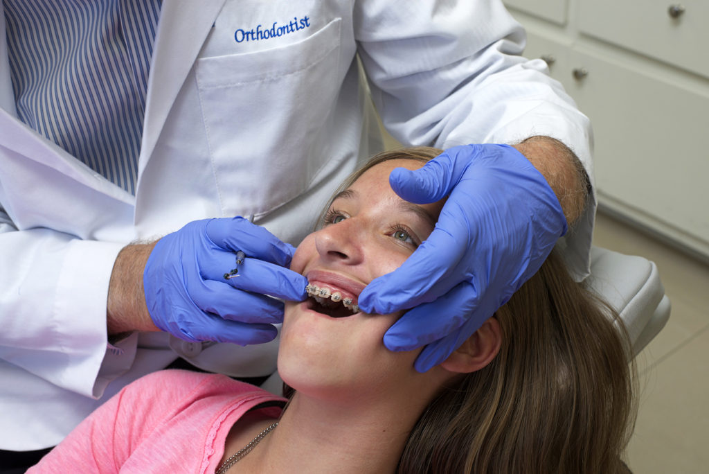 smiling girl having her braces checked by orthodontist